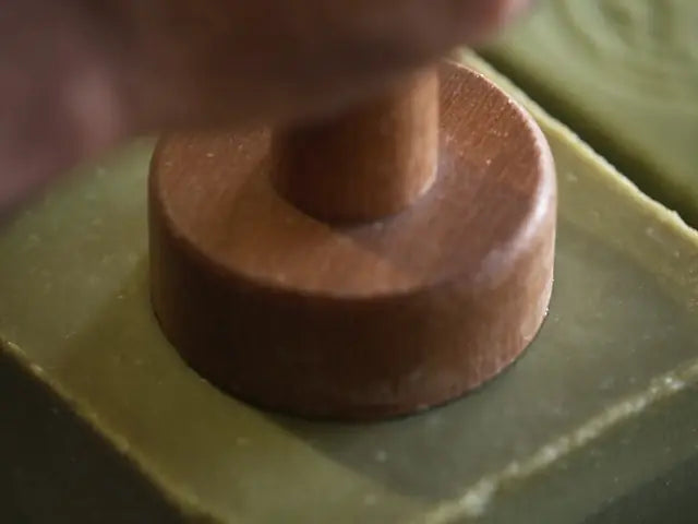 A maker pressing a stamp into a bar by hand